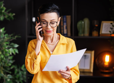 Middle aged businesswoman making phone call in home officeの写真素材