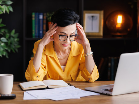 Overwhelmed businesswoman suffering from headache in home officeの写真素材