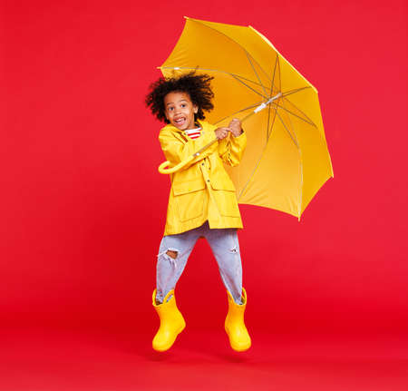 Cheerful happy ethnic boy jumping with umbrellaの写真素材