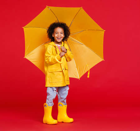 Cheerful ethnic boy standing with umbrella against red backdropの写真素材