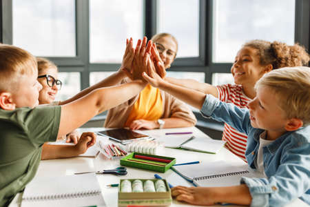 Teacher and joyful students celebrate successful completion of collective school work in a bright classroomの写真素材