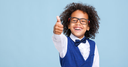 Happy ethnic schoolboy in formal suit and glasses approving school educationの写真素材
