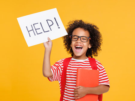 Happy ethnic schoolboy holds a sign HELP and book and laughsの写真素材