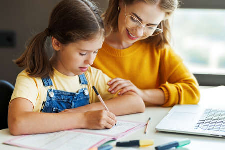 Cheerful mother doing homework with daughter at homeの写真素材
