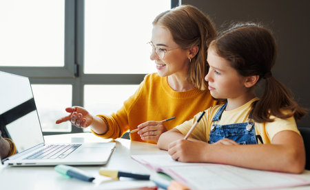 Cheerful mother doing homework with daughter at homeの写真素材