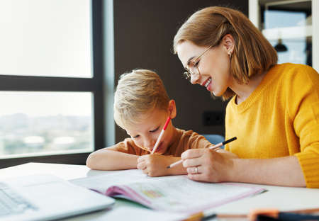Cheerful mother doing homework with son at homeの写真素材