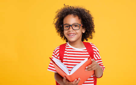 Happy ethnic schoolboy laughing with book against yellow backgroundの写真素材