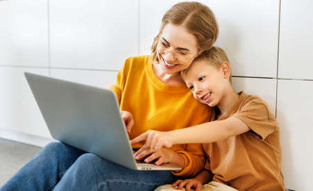 Cheerful boy using laptop with mom and watching funny videos on laptop together at homeの写真素材