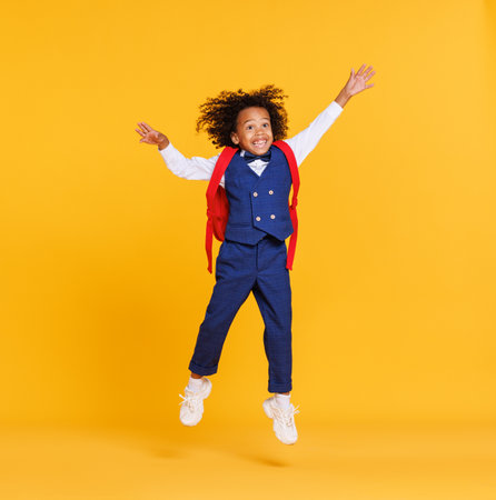 Energetic ethnic stylish schoolboy jumping against yellow backdropの写真素材