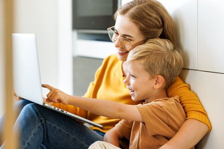 Cheerful boy using laptop with mom and watching funny videos on laptop together at homeの写真素材
