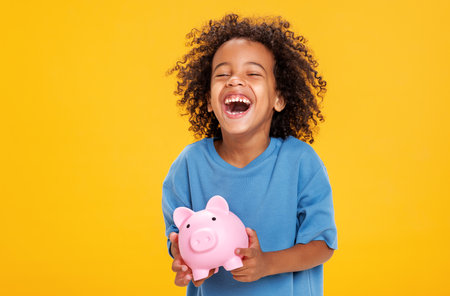 Happy ethnic boy storing money in piggy bankの写真素材