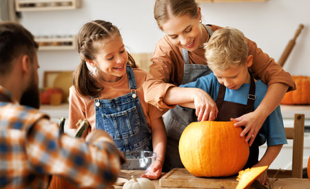 Happy family mother, father and kids to remove pulp from from pumpkin while carving jack o lantern with familyの写真素材