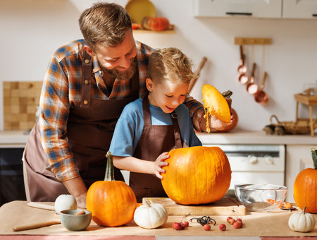 Son and dad making Jack-o-Lantern together at home, carving Halloween pumpkinの写真素材