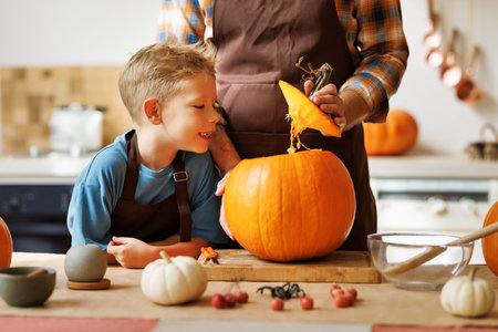 Son and dad making Jack-o-Lantern together at home, carving Halloween pumpkinの写真素材