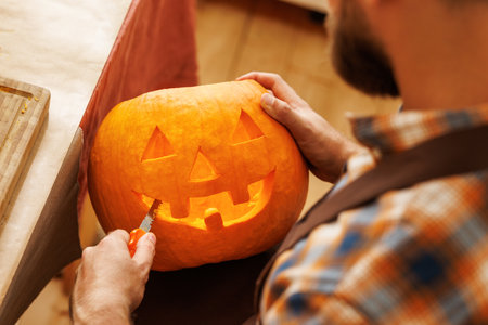 Cropped shot of man carving large orange pumpkin while preparing for Halloween partyの写真素材