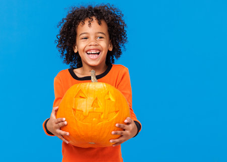 Happy cheerful ethnic boy in a pumpkin costume celebrates Halloween and laughs on a bright blue backgroundの写真素材