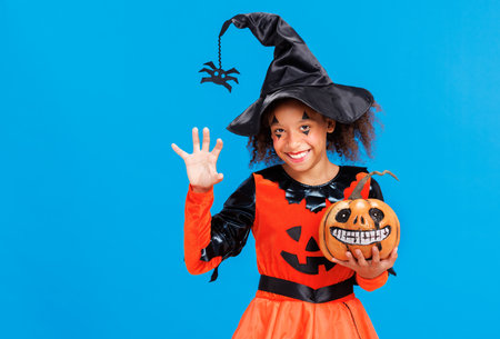 Happy cheerful ethnic girl in a pumpkin costume scary gestures and celebrates Halloween and laughs on blue backgroundの写真素材