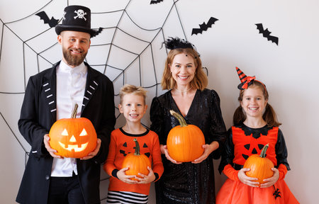 Cheerful family in carnival costumes celebrate Halloween near a gray wall with cobwebs and batsの写真素材