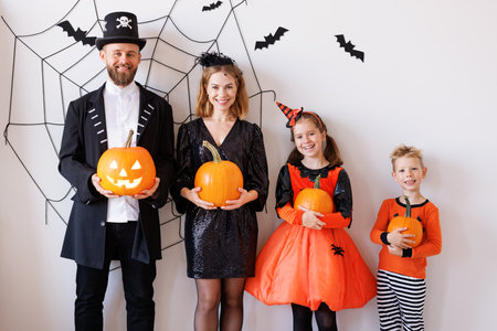 Cheerful family in carnival costumes celebrate Halloween near a gray wall with cobwebs and batsの写真素材