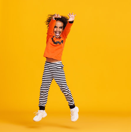 Happy ethnic boy in pumpkin costume jumping and celebrates Halloween on yellow backgroundの写真素材