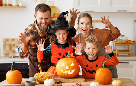 Happy family parents and kids does scary gesture, while make jack-o-lantern from pumpkin, getting ready for halloweenの写真素材