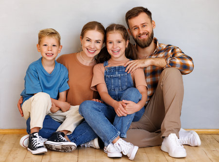 Happy family mother father and children sitting on floor against empty grey wallの写真素材
