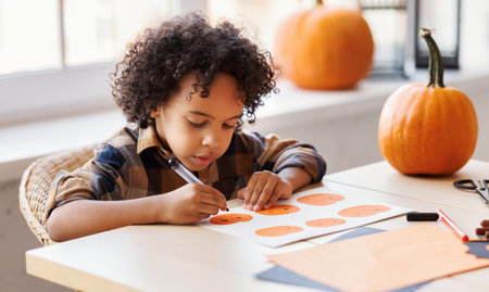 Cute ethnic child boy making Halloween home decorationsの写真素材