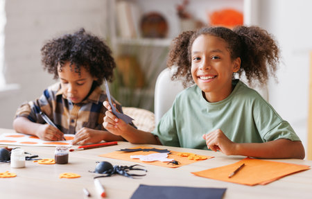 Happy ethnic children girl and boy making Halloween home decorations togetherの写真素材