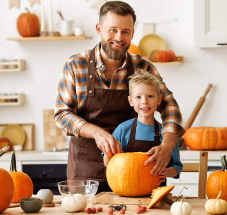 Son and dad making Jack-o-Lantern together at home, carving Halloween pumpkinの写真素材