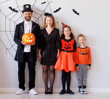 Cheerful family in carnival costumes celebrate Halloween near a gray wall with cobwebs and batsの写真素材