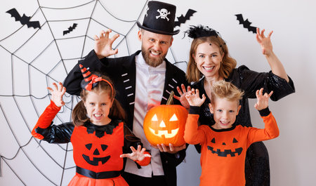 Cheerful family in carnival costumes celebrate Halloween and does scary gesture near gray wall with cobwebs and batsの写真素材