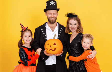 Cheerful family in carnival costumes celebrate Halloween on colored yellow backgroundの写真素材