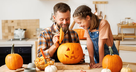 Daughter and dad making Jack-o-Lantern together at home, carving Halloween pumpkinの写真素材