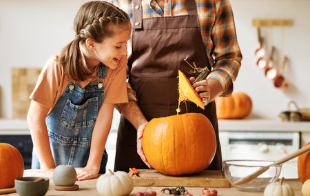 Daughter and dad making Jack-o-Lantern together at home, carving Halloween pumpkinの写真素材