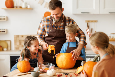 Happy family mother, father and kids to remove pulp from from pumpkin while carving jack o lantern with familyの写真素材