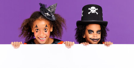 Happy Halloween. African american children in carnival costumes and makeup with blank white poster on colored purple backgroundの写真素材