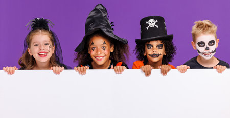 Happy Halloween. Group of children in carnival costumes and makeup with blank white poster on colored purple backgroundの写真素材
