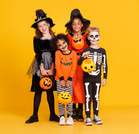 Happy Halloween. Cheerful kids in carnival costumes and makeup with pumkin pumpkin basket smiling on bright colored yellow backgroundの写真素材