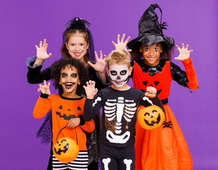Happy Halloween. Cheerful kids in carnival costumes and makeup make a terrible on bright colored purple backgroundの写真素材