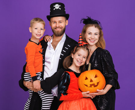 Cheerful family in carnival costumes smiling and celebrate Halloween with jack-o-lantern on colored purple backgroundの写真素材