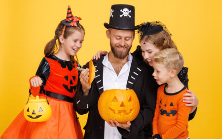 Cheerful family in carnival costumes celebrate Halloween with jack-o-lantern on colored yellow backgroundの写真素材