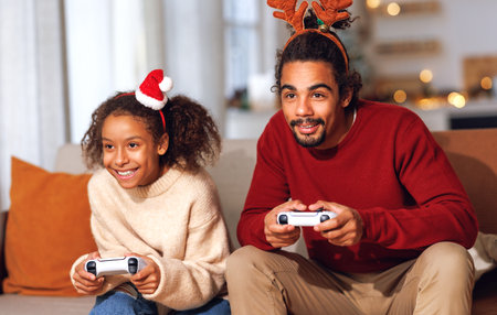 Happy ethnic african american family father and daughter laugh and play video games together using a video game console n christmas holidayの写真素材