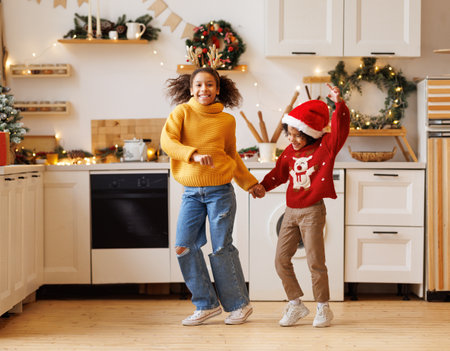 Happy positive african american kids boy and girl have fun on Christmas day at home. Siblings children dance to New Year music during winter holidaysの写真素材