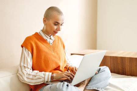 Beautiful woman freelancer with short hair works, while sitting on sofa and resting on laptop during work from home in daytimeの写真素材