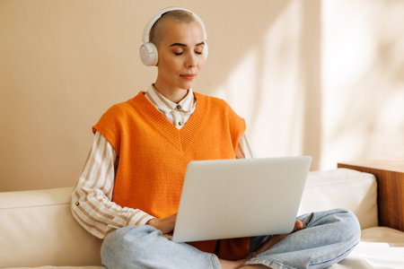 Beautiful woman freelancer in headphones with short hair works, while sitting on sofa and working on laptop during work from home in daytimeの写真素材