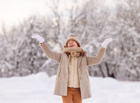 Happy excited kid in warm clothes enjoying snow falling on face while playing in snowy park or forest, little girl having fun outdoors during first snowfall. Outdoor fun winter activities for childrenの写真素材