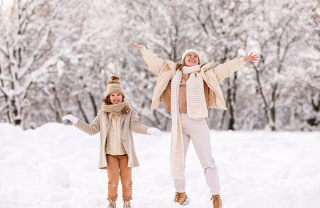 wintertime. Happy family mother and child rejoicing first snow and having fun outdoors in snowy winter park, excited overjoyed kid daughter and mom playing together on frosty day in forestの写真素材