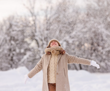 Happy excited kid in warm clothes enjoying snow falling on face while playing in snowy park or forest, little girl having fun outdoors during first snowfall. Outdoor fun winter activities for childrenの写真素材