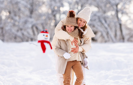 Lovely happy family, mother and little girl daughter have fun during snowy weather outdoor. Young positive mom embrace kid while playing on fresh frosty air in winter park, selective focusの写真素材