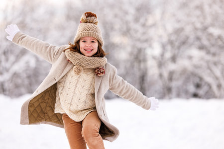 Happy excited little girl in warm clothes happily playing in winter park, kid running through snow with arms outstretched and joyfully laughing. Fun outdoor activities for children in wintertimeの写真素材